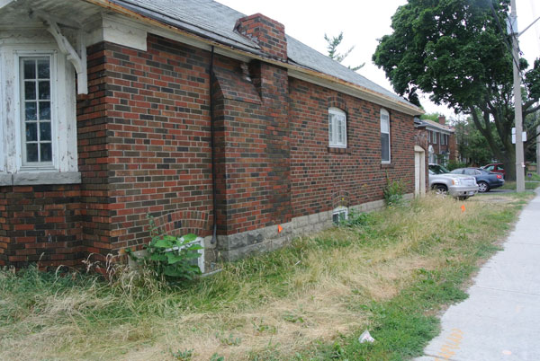 A sad case of neglect – a property standards issue (rusted eavestrough, peeling, flaking paint, chimney with a few bricks short of a load, turf grass left to overgrow and weeds appearing).